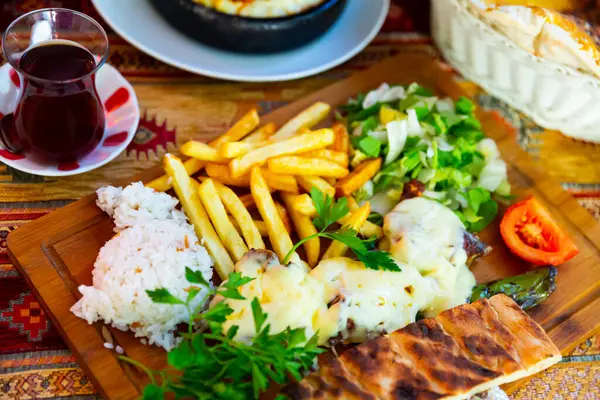 Baked ribs with cheese garnished with rice, french fries and vegetables on a wooden board. Turkish cuisine