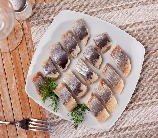 淡盐水鲱鱼片排成整齐的一排 放在盘子里 在木制的桌子上有一个盘子 上面摆满了鱼子酱和欧芹 — 图库照片