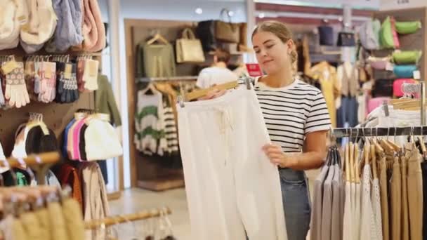 Νεαρή Γυναίκα Αγοραστής Στο Κατάστημα Έχει Αφαιρεθεί Κρεμάστρα Παντελόνι Από — Αρχείο Βίντεο