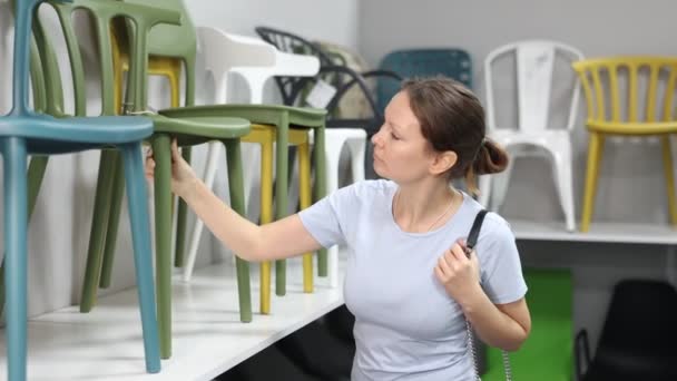 家具店では オフィススイートを完成させるために椅子を選択することを検討している女性 背部が付いているプラスチックおよび木の椅子 オフィスの座席 — ストック動画