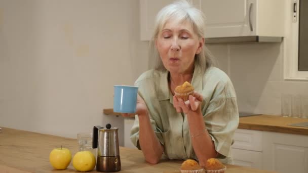 Θετική Γριά Γυναίκα Πίνει Καφέ Και Τρώει Κεκάκια Στην Κουζίνα — Αρχείο Βίντεο