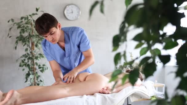 治療室の若い女性のための脚マッサージ手順を実施する熟練した男性の理学療法士 — ストック動画