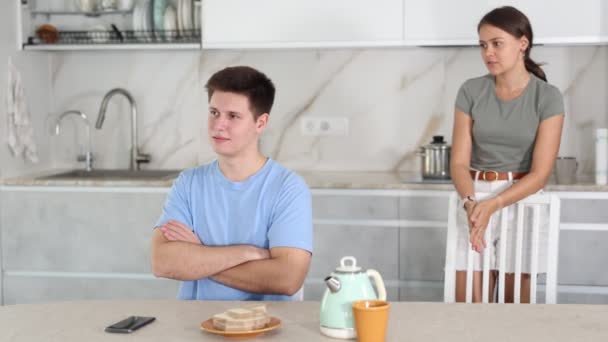 失望した若い男は 関係の問題に直面し キッチンテーブルに座って 不満のガールフレンドは ぼやけた背景に彼を叱る — ストック動画
