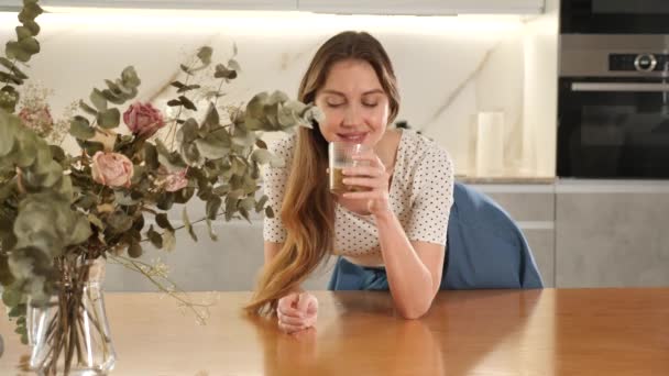 中年妇女喝卡布奇诺咖啡 坐在厨房的桌子上 手里拿着白色的家具 — 图库视频影像