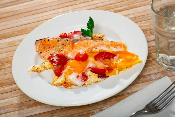 Dish of tasty scrambled eggs with salmon and tomatoes at plate on table