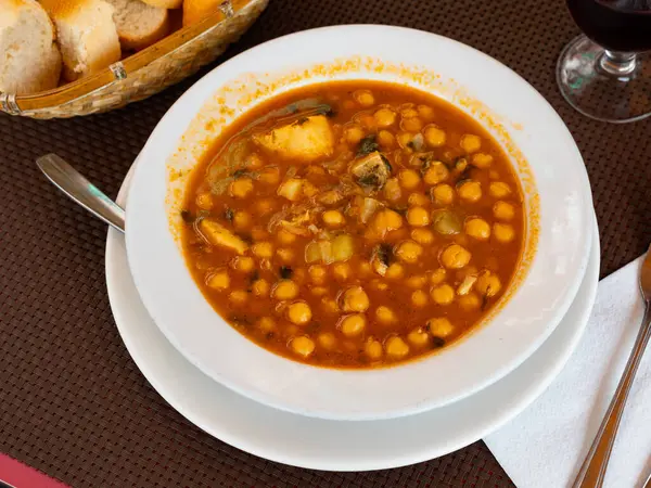 Hearty Mediterranean lunch is cooked on plate - soup stew boiled of cod fillet, potatoes, chickpeas in tomato sauce.