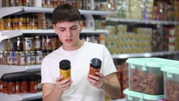 Zainteresowany Młodzieniec Rozważający Wybór Naturalnych Aromatycznych Przypraw Uważnie Czytający Etykiety — Wideo stockowe
