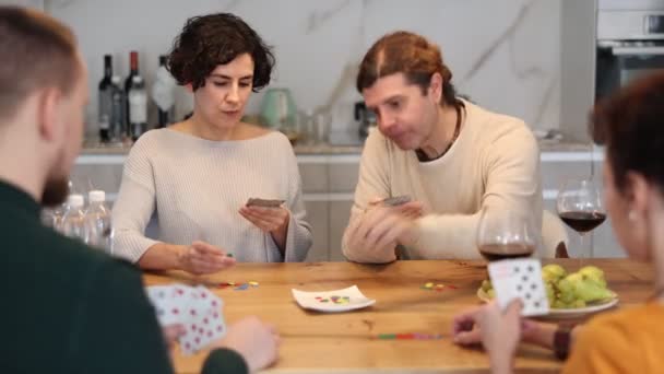 キッチンテーブルに座ってポーカーゲームを楽しむ男性と女性の陽気なフレンドリーな会社 友人は家でカードゲームをする イブニングエンターテインメントコンセプト — ストック動画