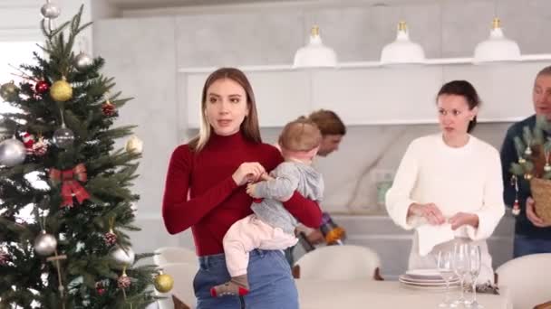 Kollarında Bebek Olan Genç Bir Kadın Noel Ağacını Oyuncaklarla Süslerken — Stok video