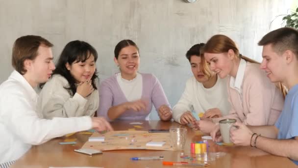 陽気な感情的な女の子と男の子 学生の友人のグループ テーブルの周りに集まって 余暇の時間に面白いボードゲームをプレイ — ストック動画