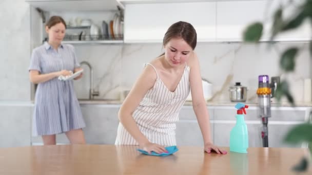 ポジティブな若い女の子はテーブルの表面をきれいにする キッチンでタオルが付いている母の乾燥皿 — ストック動画