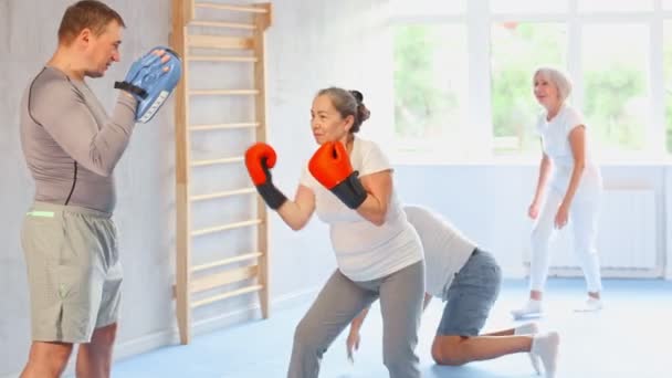 上了年纪的女人和她的教练在体育馆里戴拳击手套的女人练习拳击 冲到垫子上打拳击 高质量的4K镜头 — 图库视频影像