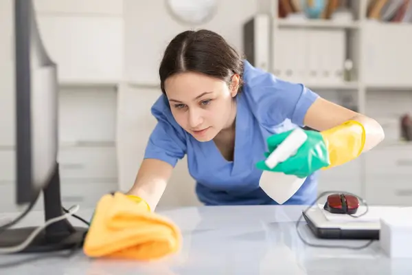Cleaning company employee wipes dust from table in office