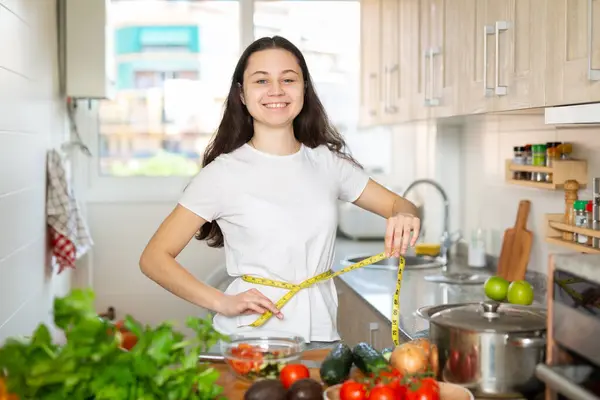 年轻的漂亮姑娘在厨房里用尺子量她的腰围 饮食与体重减轻概念 — 图库照片