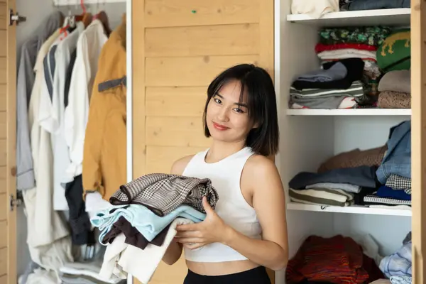Iloinen Nuori Aasialainen Nainen Poseeraa Vaatekaappi Tilalla Taita Vaatteita Yhdellä — kuvapankkivalokuva