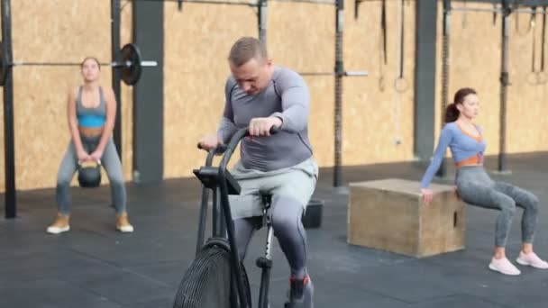 心臓トレーニングを行っているポジティブな集中運動大人の男性 ジムの静止エアバイクでサイクリング スポーツとフィットネスのコンセプト 高品質の4K映像 — ストック動画