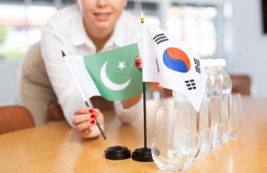 Preparation for international negotiations. Office coordinator setting national flags of South Korea and Islamic Republic of Pakistan on table, cropped shot. Concept of bilateral diplomatic relations clipart