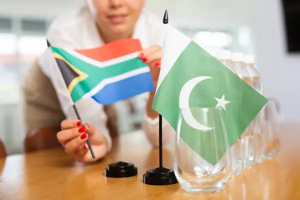 南アフリカの水と旗のボトルが付いているテーブルの上のパキスタンの小さな旗は会議室の肯定的な若い女性によってそれを隣に置きました — ストック写真