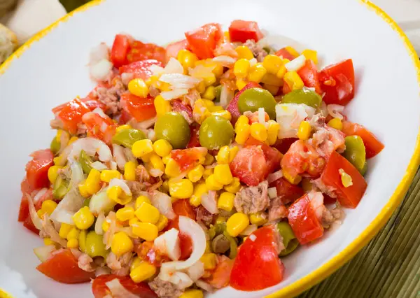 Plate of tasty salad with tuna, canned corn, tomatoes, olives and onion