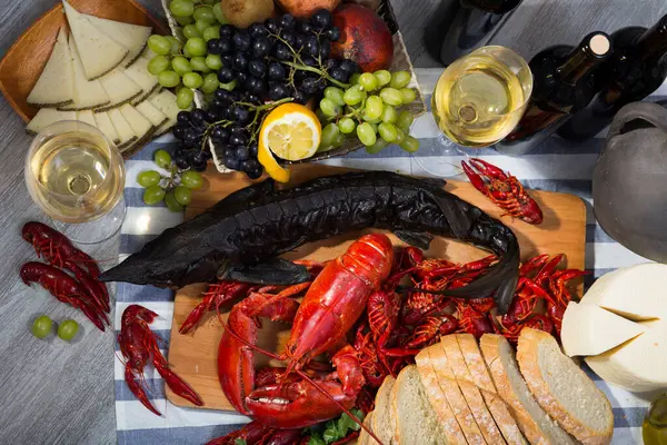 Top view of smoked sturgeon and boiled lobster with crayfishes, fruits and white wine on wooden table