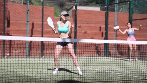 阳光明媚的日子 两个年轻的女运动员在法庭上玩羽毛球 — 图库视频影像
