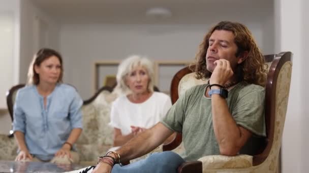 法律上の母親と妻が彼に同意しないとき リビングルームに椅子に座っているかわいい男性 — ストック動画