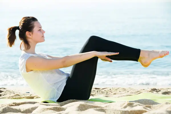 身穿白色T恤的成年女性正在海滩上练习瑜伽 图库照片