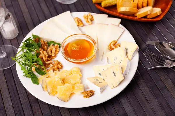 Delicious tasty cheese dish for romantic dinner, assorted cheese with nuts and honey on white plate