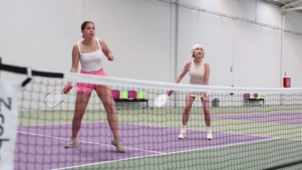 具有表现力的年轻女运动员在室内场地与经验丰富的女伴玩双打泡菜球 准备击球 体育情绪的概念 视频剪辑
