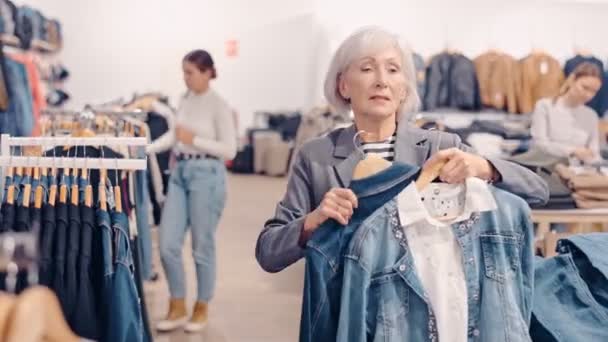 Mulher Idosa Comprador Escolhe Jaqueta Jeans Loja Roupas — Vídeo de Stock