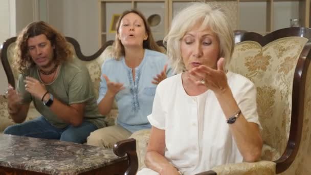 不满意的岳母坐在椅子上 在家里客厅的沙发上 面对着一个困惑的丈夫和妻子 图库视频片段