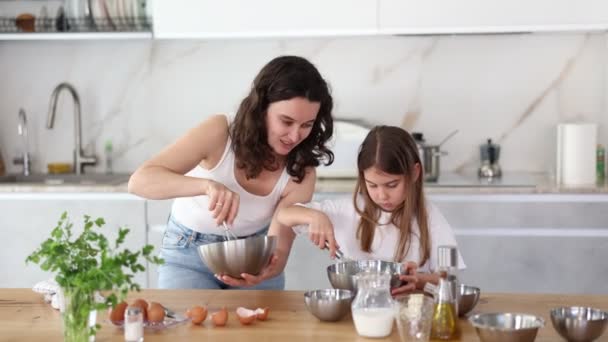 ママは娘にデザートを作る方法を教え ウィスキーで生地を打つ方法を示しています ママと女の子はキッチンで話し ウィスキーとボウルのペストリーのための成分を混ぜています — ストック動画