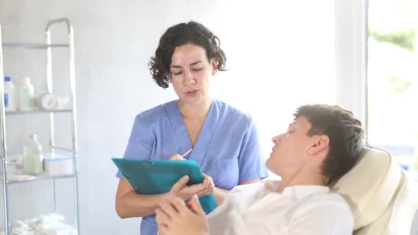 Junger Mann Sitzt Auf Stuhl Bei Einem Arzttermin Mit Kosmetikerin — Stockvideo