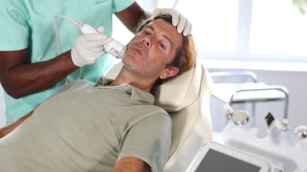Mannen Ligger Soffan Ansiktets Hudvårdsprocedur Afrikansk Kosmetolog Läkare Med Hjälp — Stockvideo