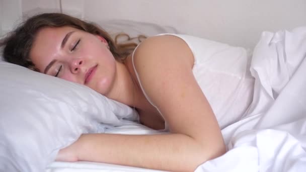迷人的女孩 一头长长的棕色波浪般的秀发睡在她家床上的白色床单上 — 图库视频影像