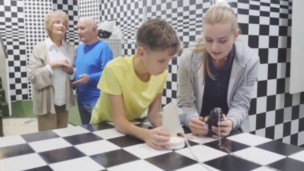 脱出室に立ちながらチェスの謎を解く少年少女 祖父と祖母が背景に立ってそれらを見て — ストック動画