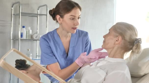 老年妇女在临床椅子上照镜子时 与专家进行面部美容美感咨询 — 图库视频影像