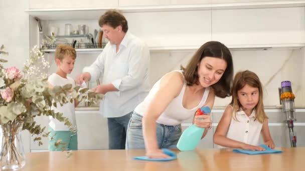 ポジティブな母親と娘はキッチンテーブルの表面を掃除し 他の家族はキッチンで異なる宿題をしている — ストック動画