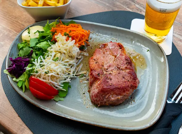伝統的なベルギーのグリルポークステーキのバーケンコート ロスは ビール フライドポテトとマヨネーズソースと新鮮な野菜の野菜のガーニッシュを提供しています ロイヤリティフリーのストック写真