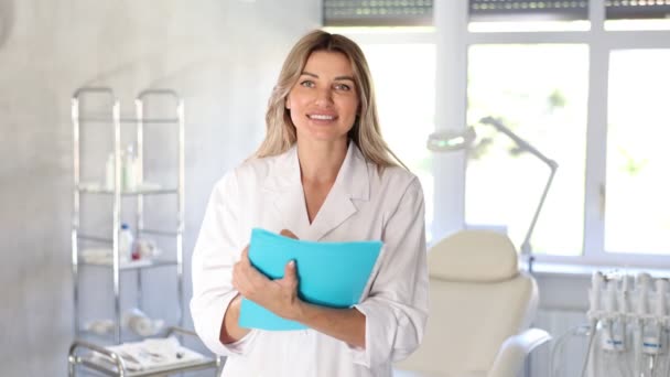 Üniformalı Gülümseyen Kadın Doktor Klinikte Duruyor Dosyasını Tıbbi Kayıtlarla Dolduruyor — Stok video