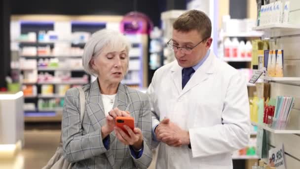 Ενδιαφερόμενη Ηλικιωμένη Πελάτισσα Ρωτάει Μεσήλικες Χημικούς Για Προϊόν Που Αντανακλάται — Αρχείο Βίντεο