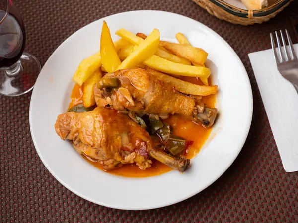 European cuisine restaurant serves spicy toasted chicken thigh with chili and chicken fixings. Meat is complemented with French fries and beer. Rustic dinner - fried poultry with garnish and bread.