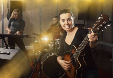 Group of young musicians with passionate emotional female vocalist and guitarist rehearsing in recording music studio clipart