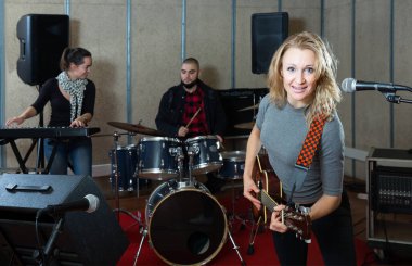 Rehearsal of music band. Joyful female guitar player and singer practicing with band members in recording studio clipart