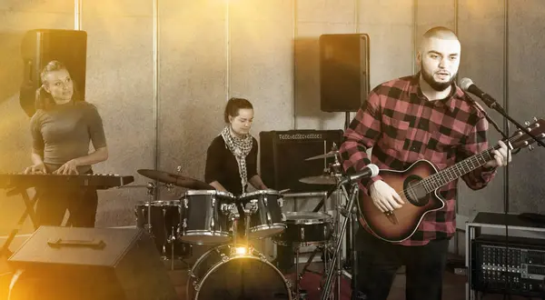 stock image Rehearsal of music band. Happy cheerful guy guitar player and singer practicing with band members in recording studio