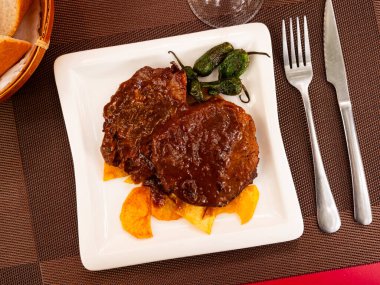 Tasty baked beef steak in fragrant gravy served with potatoes at white plate. Traditional Spanish dish clipart