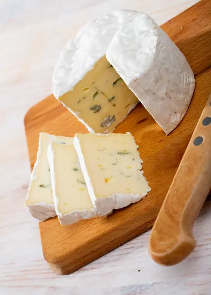 Stock image Wheel of delicate blue cheese with cut slices on wooden cutting board..