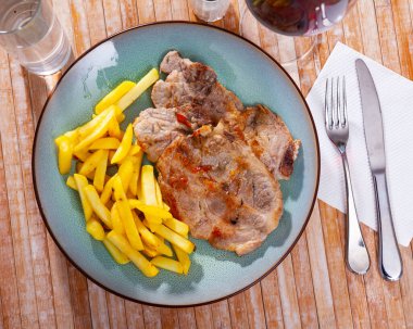Pork chop with fried French fries on a plate. clipart