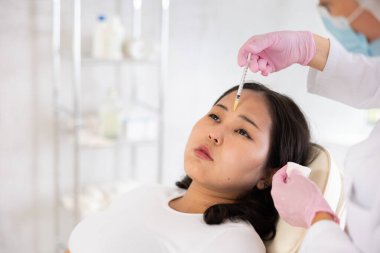 Closeup face of young female client receiving injections during lip enhancement procedure, professional cosmetologist hands in rubber gloves holding syringe clipart