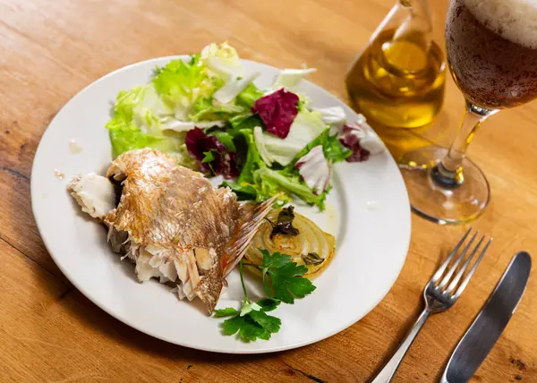 stock image Served on white plate, piece of roasted alfonsino fish pairing delightfully with caramelized onion and fresh green salad, perfect for refined dinner